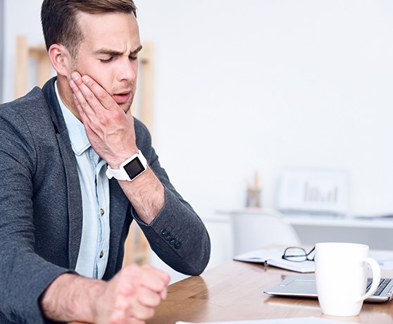 Man sitting at his desk and rubbing his aching tooth