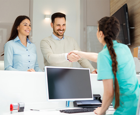 Man and woman smiling after talking to dentistry team member about dental insurance