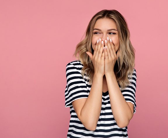 Woman laughing, covering her mouth to hide teeth