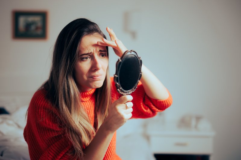 A woman looking in the mirror with a frown because gum disease is changing her face shape