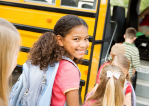 Little girl looking back and smiling as she heads towards school bus